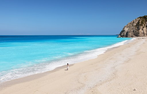 woman stands on deserted sandy beach in Greece