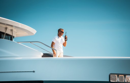 A deck crew speaks into a hand-held radio on board the bow of a yacht