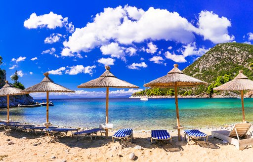 White sand beach in Greece, overlooking shallow blue waters with sun loungers and umbrellas lined up on the shore