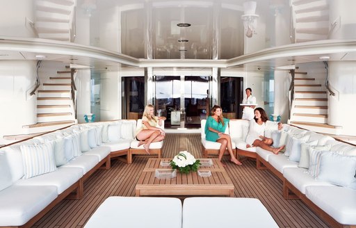 Large comfortable interior lounge on charter yacht Lady E, with light colored sofas, wooden decking and  three guests relaxing and c hatting