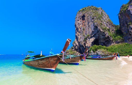 Boats on South East Asian island moored at sandy beach with rocky backdrop