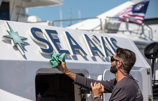 Deckhand polishing the name plate of charter yacht SEA AXIS