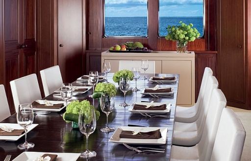 Interior dining area with table laid for a meal adjacent to large window onboard yacht charter CYAN