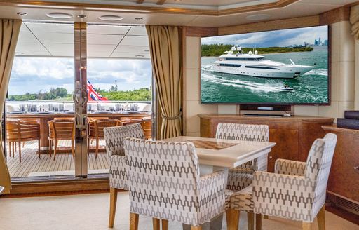 A games table with four chairs onboard charter yacht ARTEMISEA, with access to the exterior dining area visible in the background