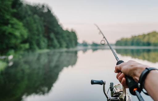 A man holds a fishing rod over mirror-calm waters in Finland