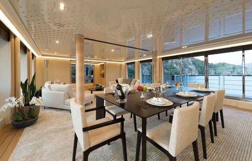 Interior dining area onboard charter yacht AQUARIUS, with full height windows to starboard and a lounge area in the background