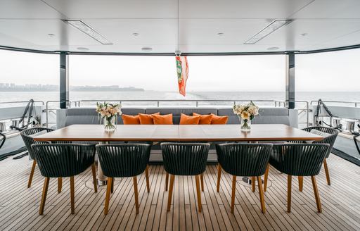 Exterior bench seating and long dining table with orange cushions onboard charter yacht HEEUS