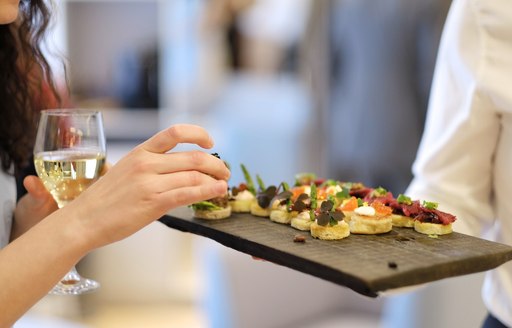 A charter guest holding a white wine glass chooses a canape on board a yacht at the Monaco Grand Prix