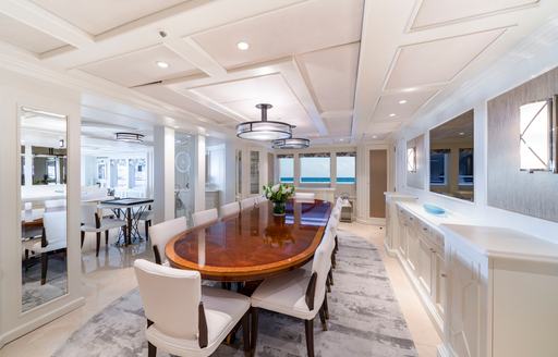 Interior dining area with long table and white seats onboard charter yacht MOSAIQUE
