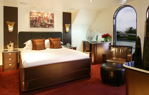 master cabin of superyacht GLOBAL, with large windows and bed with brown polished base