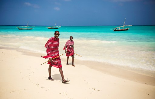 men wearing traditional swahili outfits walk on beach in tanzania 