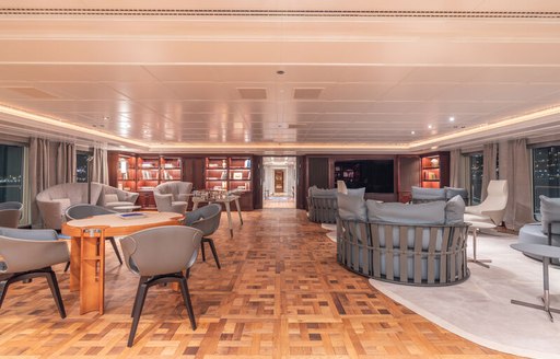 Interiors onboard charter yacht CARINTHIA VII, seating arrangements with tables to port and a white carpet and windows to starboard 