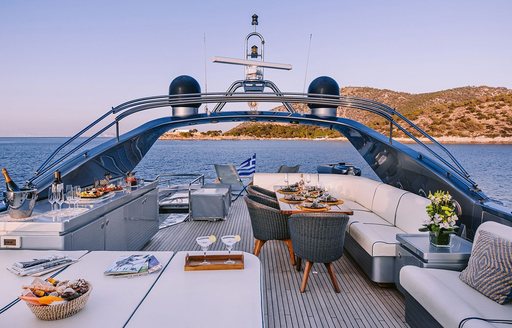 Overview of the flybridge layout onboard charter yacht ELVI, dining area center with surrounding view of the sea and an island in the background