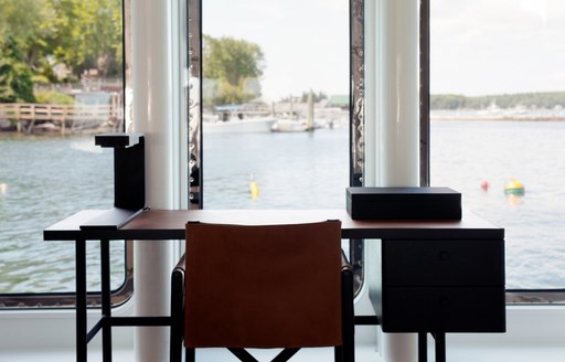 A dark wood chair tucked beneath a desk which looks out across the ocean from inside a superyacht