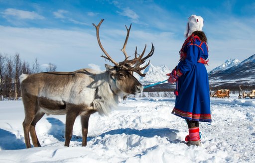 A girl dressed in traditional outfit holding the reins of a deer in Norway