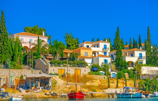 pine trees and fishing boats in front of blue and white houses on the land in greece