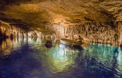 a man steers a small boat through the green waters of the Dragon caves in Mallorca, Spain