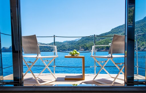 Two chairs on balcony of Interior of SANGHA superyacht looking out to clear sea with fruit in bowl on table between them