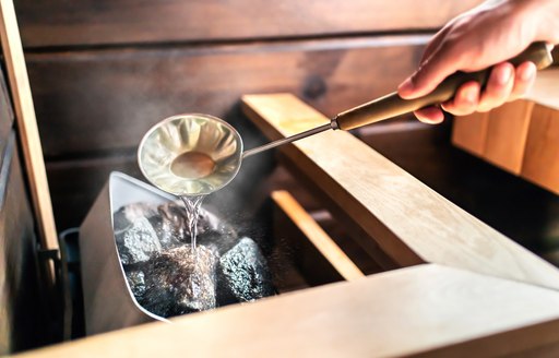 A man ladles more water into the coals of a sauna