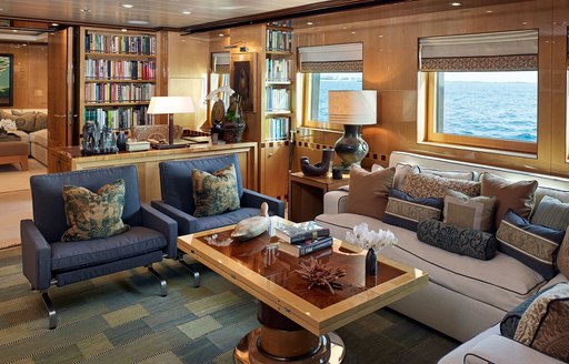 Main salon onboard Superyacht LIND, L shaped sofa and armchairs around a coffee table, with bookshelves in background