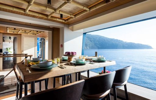 Interior dining setup onboard private yacht charter KING BENJI, rectangular table with six chairs set for a meal adjacent to a large window