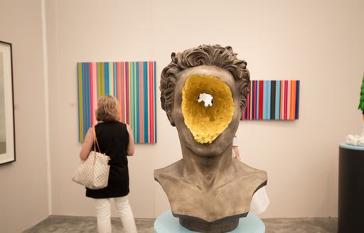 A sculpture on display at Art Basel Miami gallery, paintings in background with female charter guest viewing.