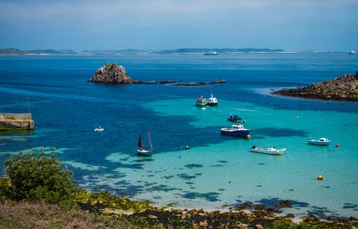 beautiful blue water of the scilly isles, with sandy seabed and little boats bobbing on the water