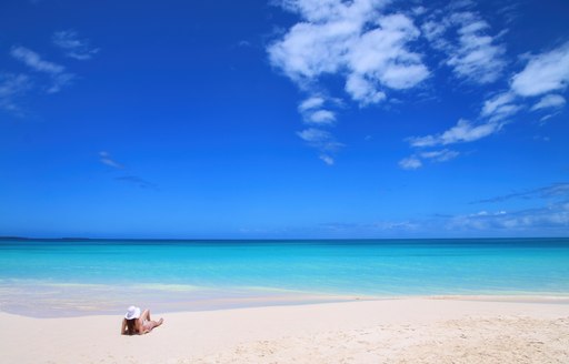 A lady sunbathing on a white sand beach with turquoise waters in the South of France