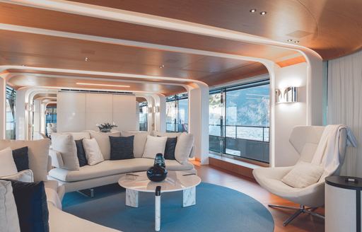 Main salon onboard yacht charter LEGEND with white seating and blue cushions, with large windows
