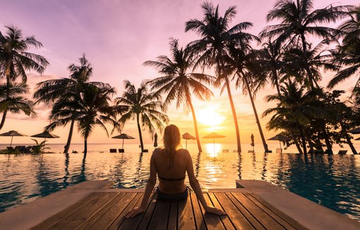 Woman relaxing by the pool in a luxurious beachfront hotel resort at sunset enjoying perfect beach holiday vacation