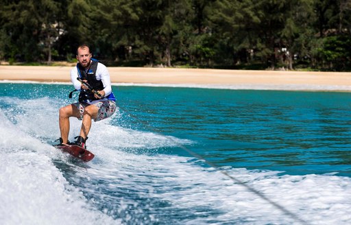 a man wake boards intensly while his yacht is anchored by a secluded beach in French Polynesia, away from the crowds of major citys and towns