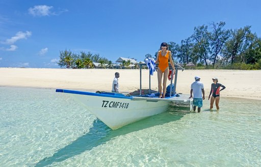 woman in yellow swimsuit stands on boat looking at the shallow water below on thanda island