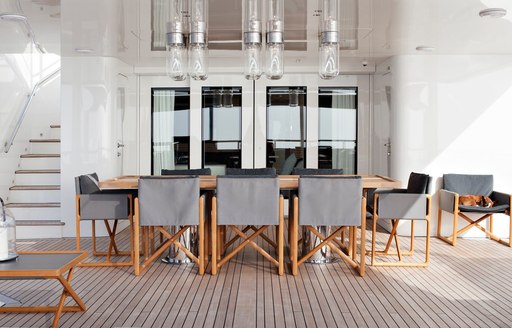 Grey chairs surround a light wood table on the exterior of a superyacht