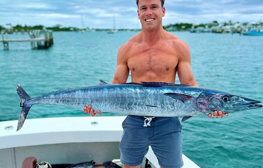 Man on fishing boat holding large fish with both hands 