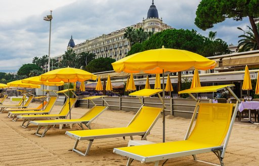 Yellow sunloungers and parasols on Cannes beach, with Carlton Hotel aft