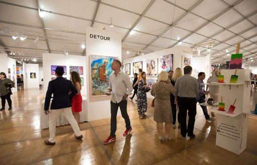 Visitors walking round exhibit in Art Basel Miami gallery, paintings on display around the room.