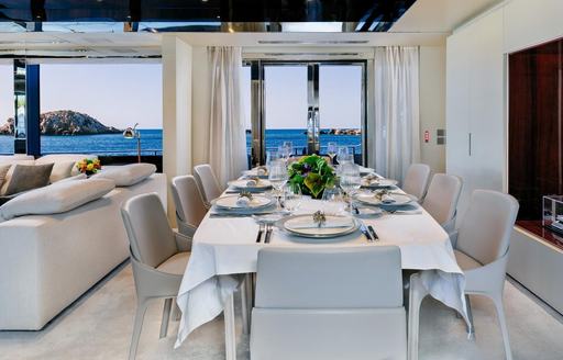 Dining table with white cover and seats adjacent to large windows onboard luxury charter yacht DON'T WORRY