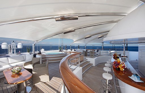 Overview of exterior deck space onboard superyacht charter OCTOPUS, with wet bar to starboard and a deck Jacuzzi with seating to port