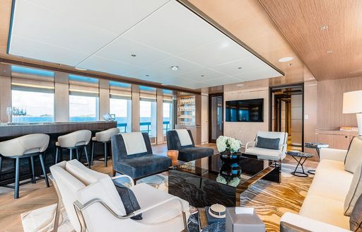 Overview of the upper salon with white and gray armchairs in the foreground and a wetbar aft onboard charter yacht MOSKITO