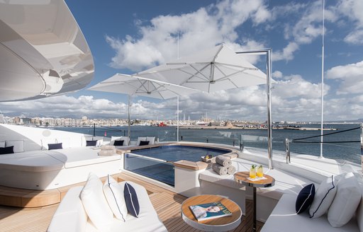 Overview of an aft deck onboard charter yacht RESILIENCE with a glass sided Jacuzzi surrounded by plush white seating and a sunpad