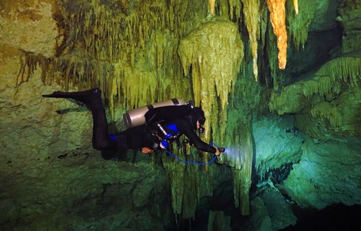 Diver swims below stalactites in blue hole