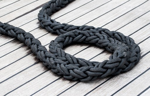 A black rope lying on a teak deck on board a superyacht