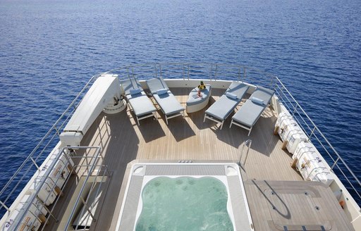 A charter guest stretching out on a sunlounger nearby to the Jacuzzi on board superyacht SERENITAS II