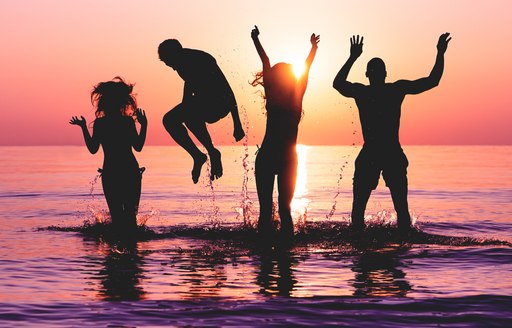 A silhouette of young revellers splashing in the sea in Ibiza at sunset