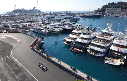 Charter yachts lining up next to racing circuit as car speeds around the track at Formula 1 Monaco Grand Prix