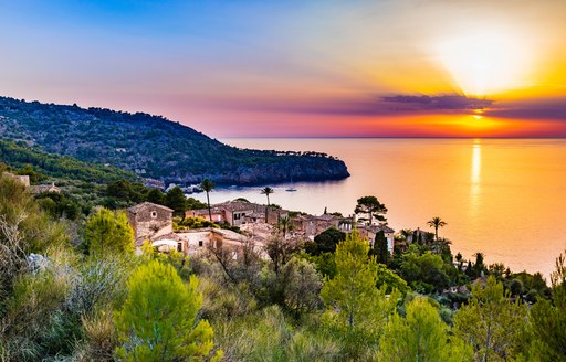 Sunset over sea in Majorca, with small village in foreground and water stretching out to horizon