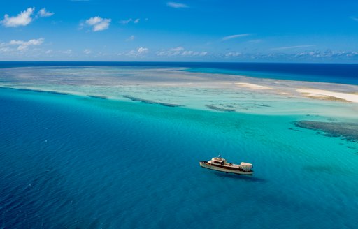 aerial view of luxury motor yacht over the rainbow off the coast of East Africa surrounded by bright blue seas with sand bar in background