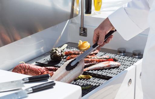 fish on barbecue grill of luxury yacht, chef picks up fillet with tongs