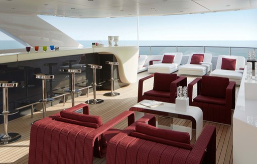 Al fresco seating onboard Charter yacht HOME, shaded armchairs and coffee tables adjacent to long bar with stools, surrounded by sea