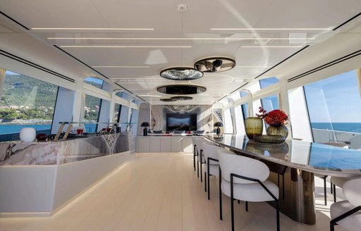 Interior dining area onboard charter yacht N1, with long table and white upholstered chairs to starboard and many windows